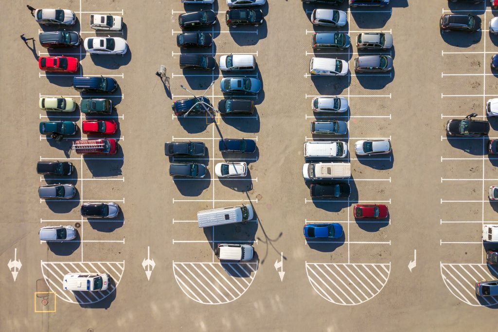 aerial view of many colorful cars parked on parking lot with lines and markings for parking places and directions