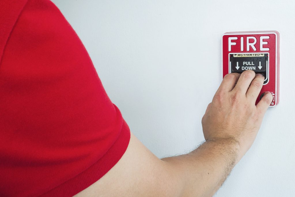 man is reaching his hand to push fire alarm hand station